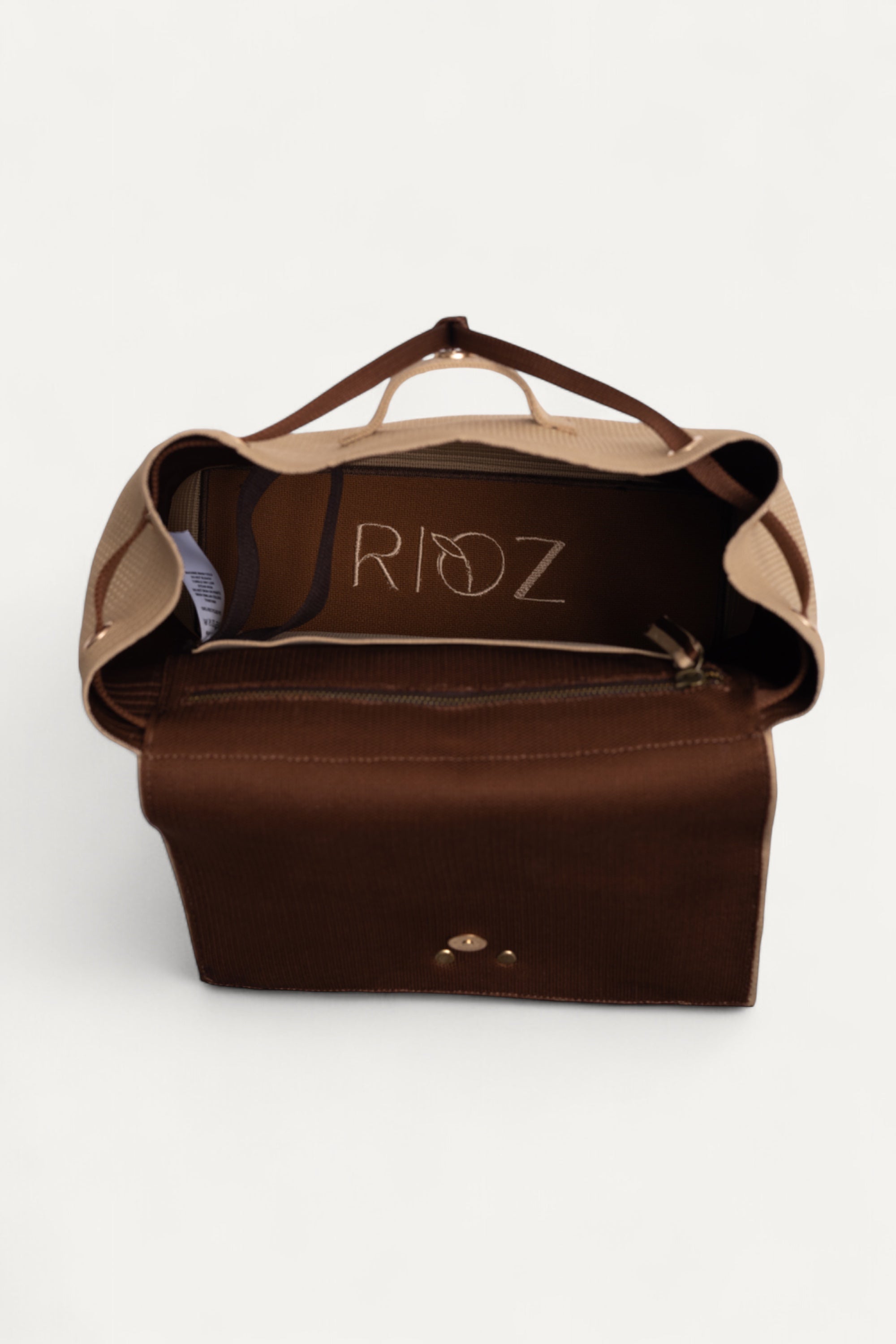 Interior view of Rioz eco-friendly backpack with brown lining and zippered pocket showing the Rioz logo; spacious, machine-washable backpack made from recycled PET bottles.