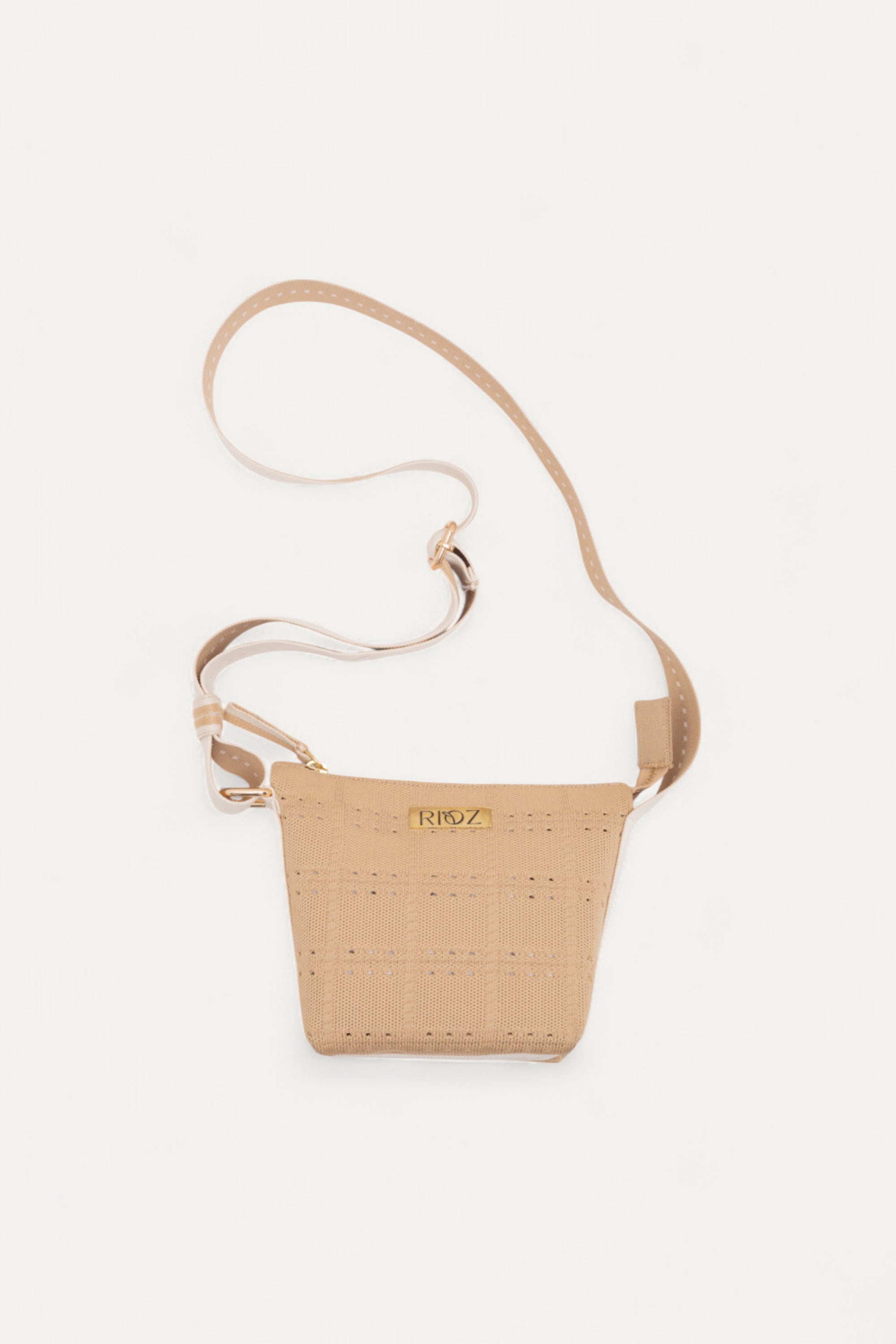 Beige crossbody bag by Rioz with wide strap and zip closure; compact, modern design perfect for daily essentials; shown on light beige background.