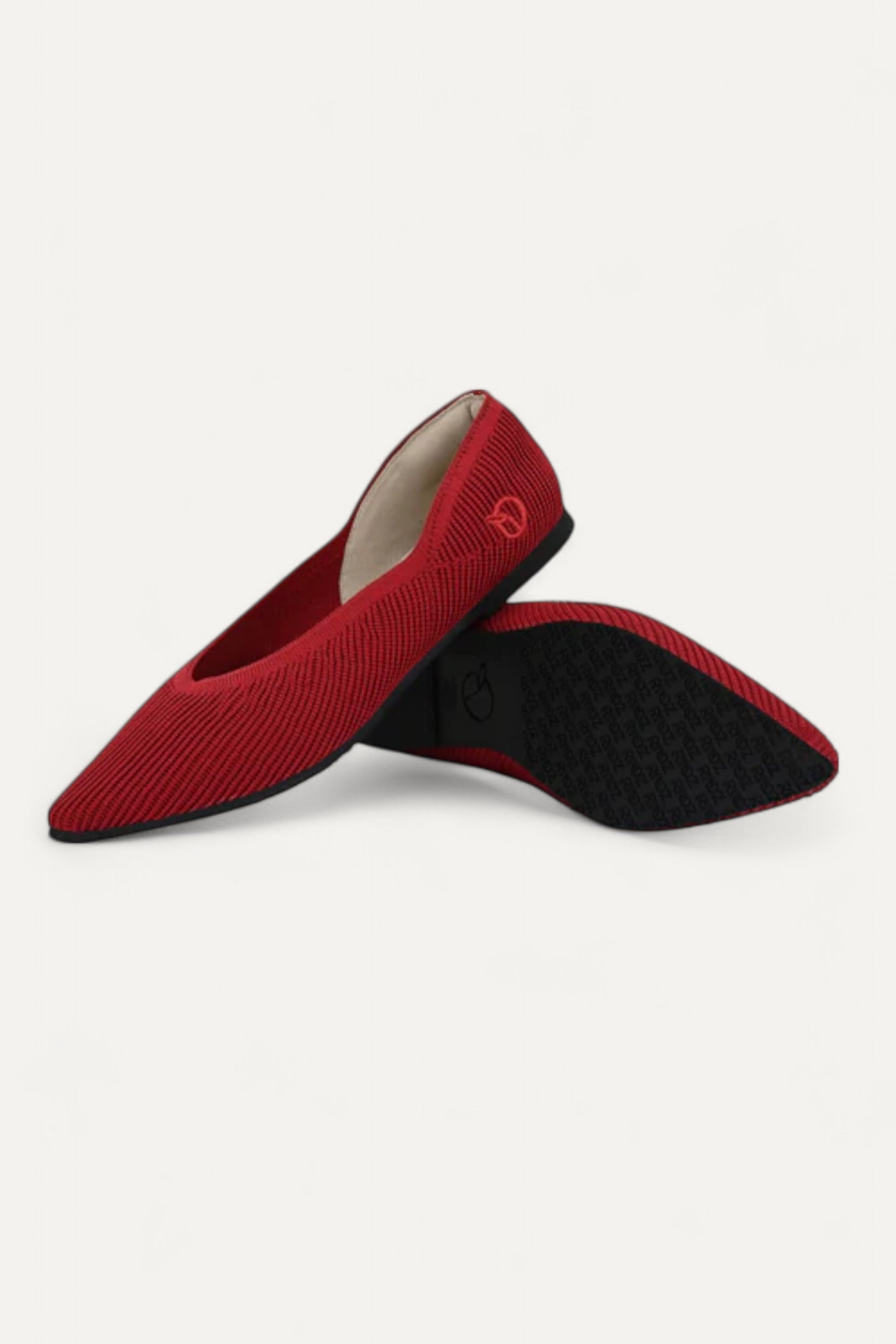 Pair of red pointed-toe ballet flats showing black sole on white background