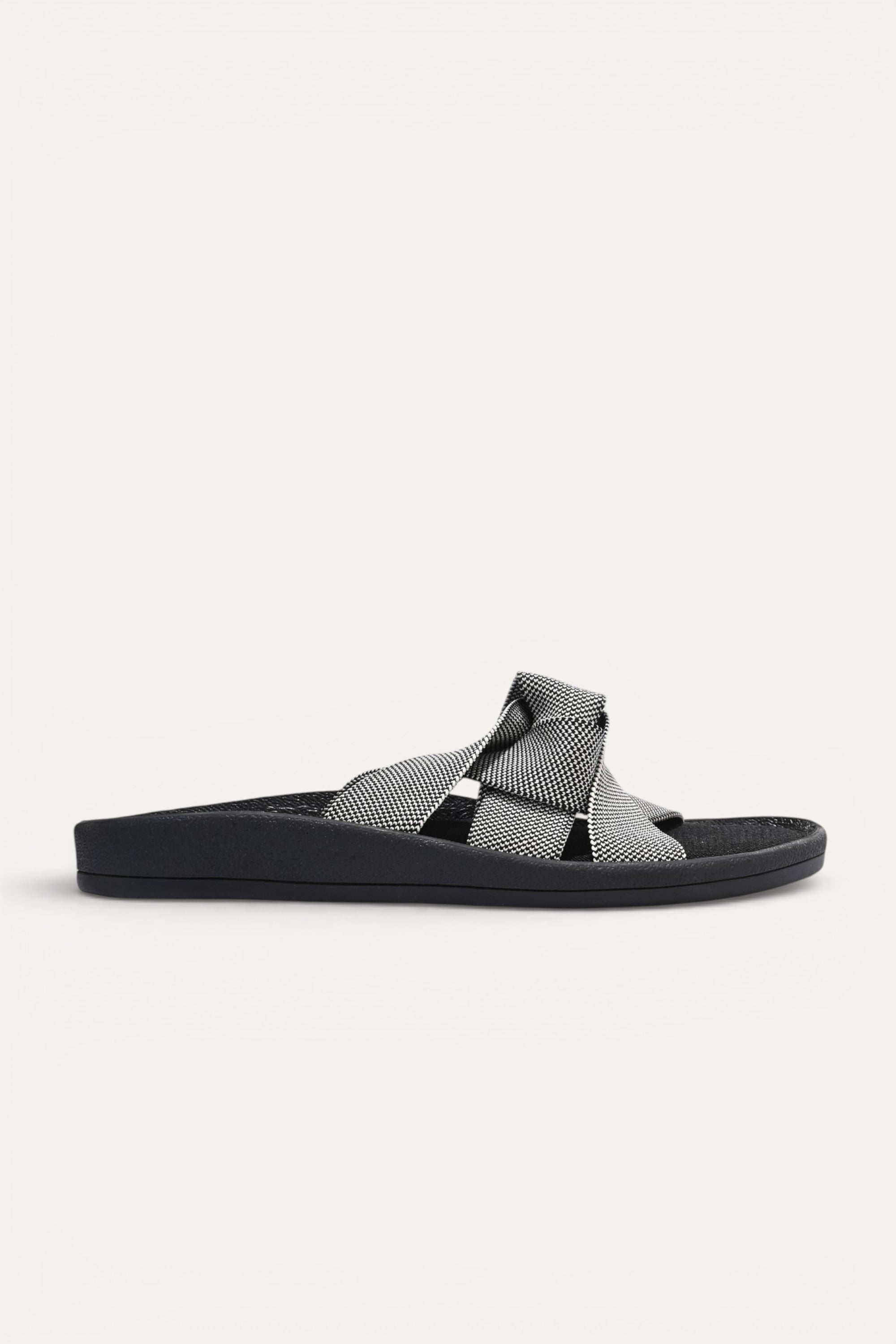 RIOZ eco-friendly slip-on sandals with grey woven bow straps, cushioned tan footbed, and brown sole, designed for lightweight everyday comfort and sustainable style.