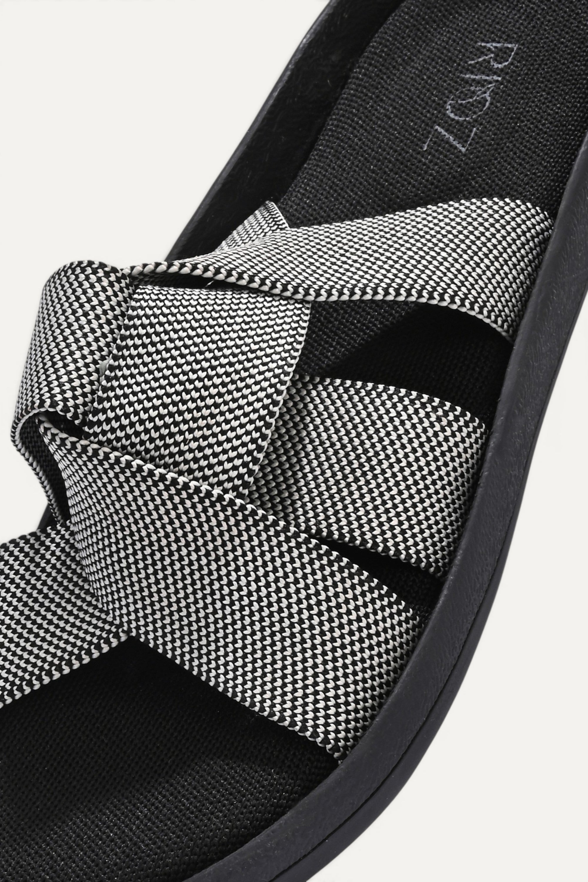 RIOZ eco-friendly slip-on sandals with grey woven bow straps, cushioned tan footbed, and brown sole, designed for lightweight everyday comfort and sustainable style.