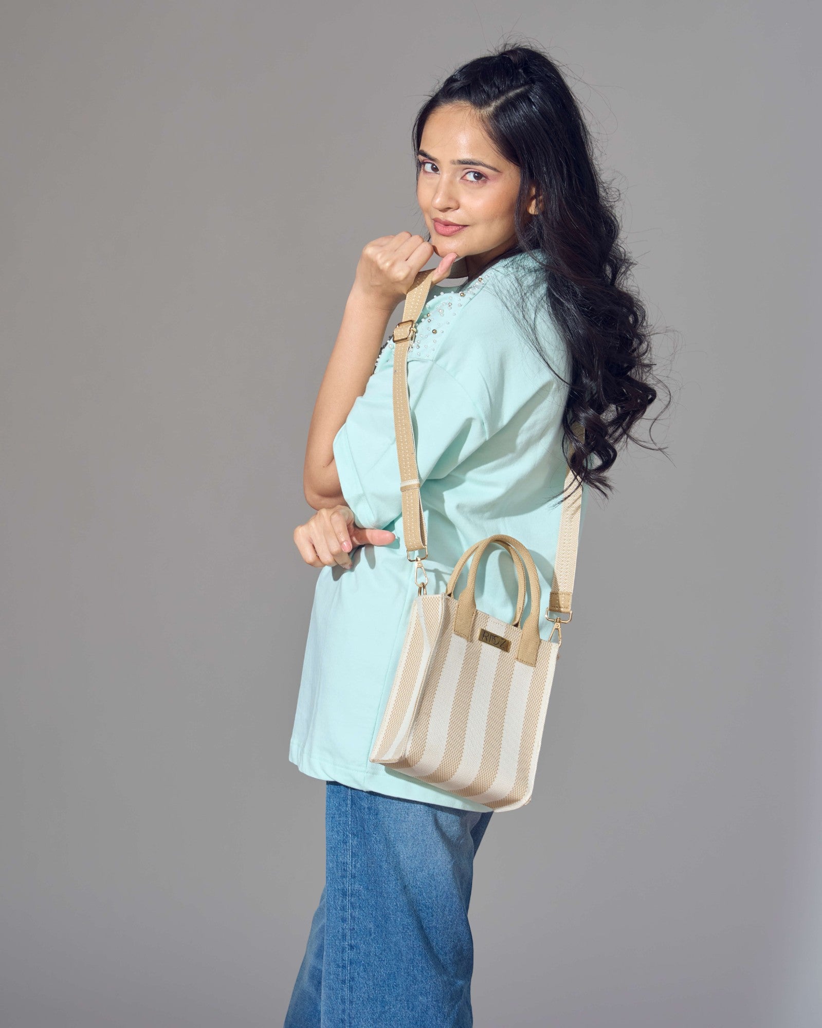 Model wearing the Midday Mini tote bag in ivory and wheat stripes by Rioz; compact, eco-friendly and lightweight crossbody bag for daily essentials.