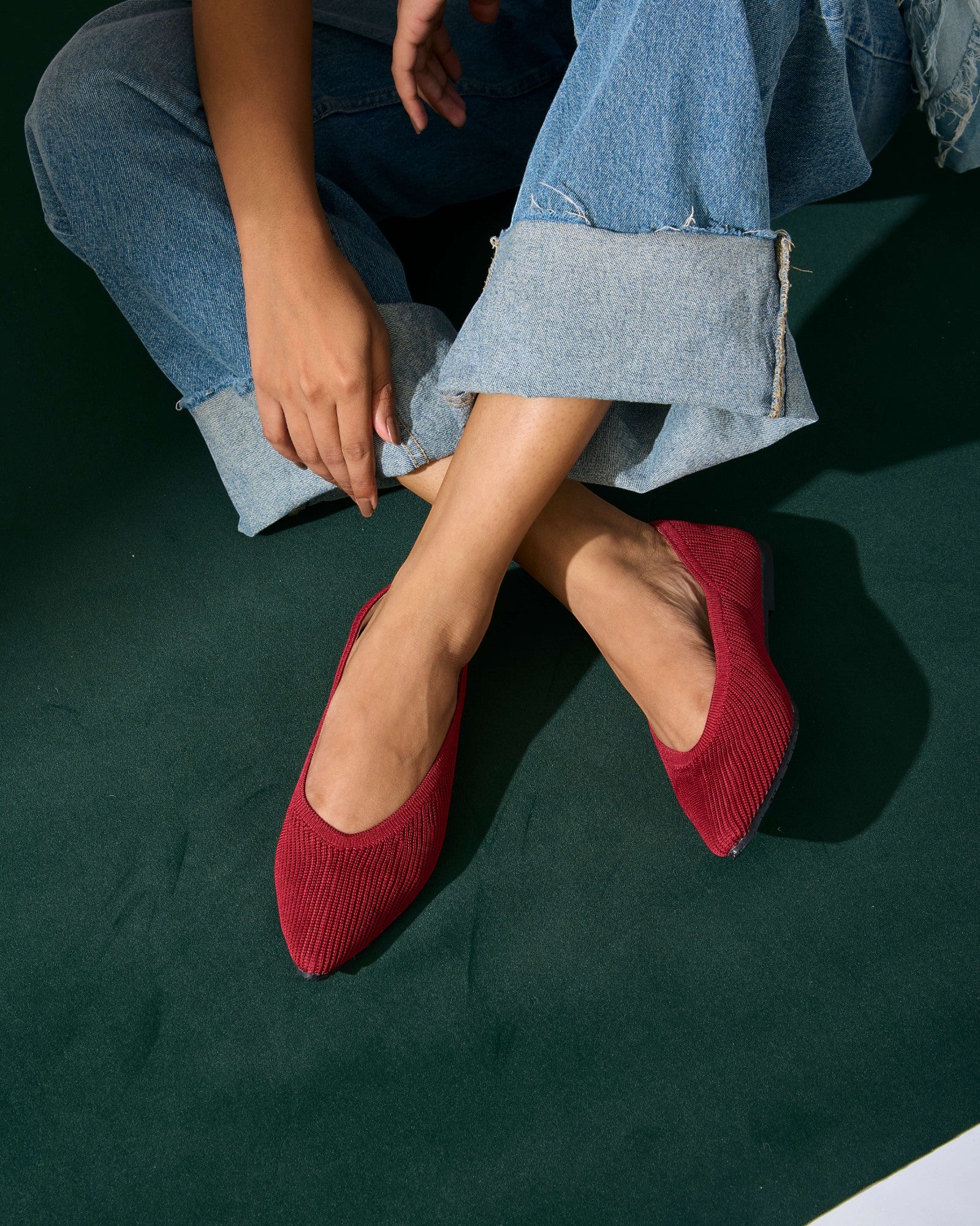 Red pointed-toe ballet flats worn with blue jeans on a dark green background