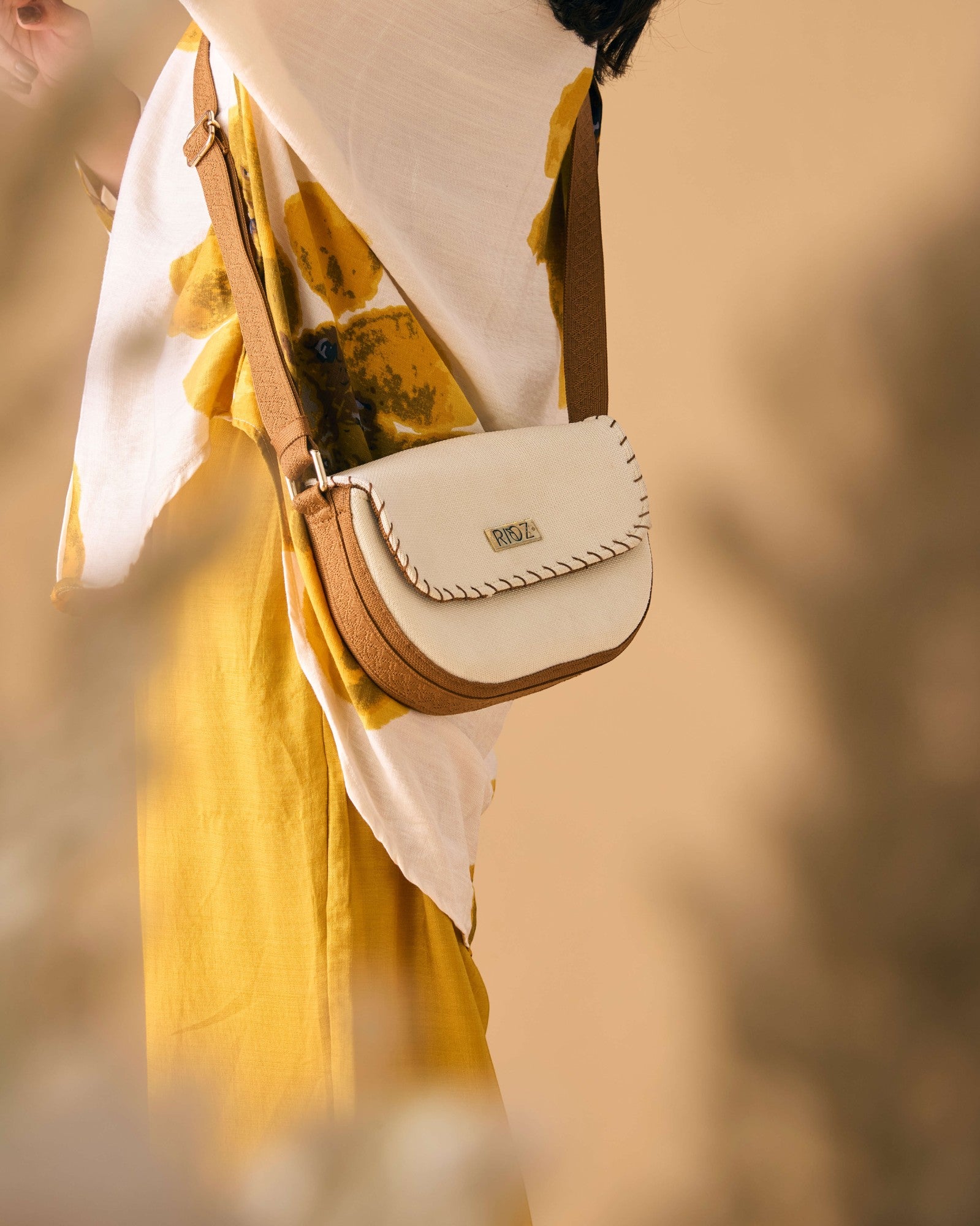Model wearing eco-friendly 9 to 9 Saddle Bag by Rioz with crossbody strap and ivory/brown body; compact, sustainable and stylish for everyday use.