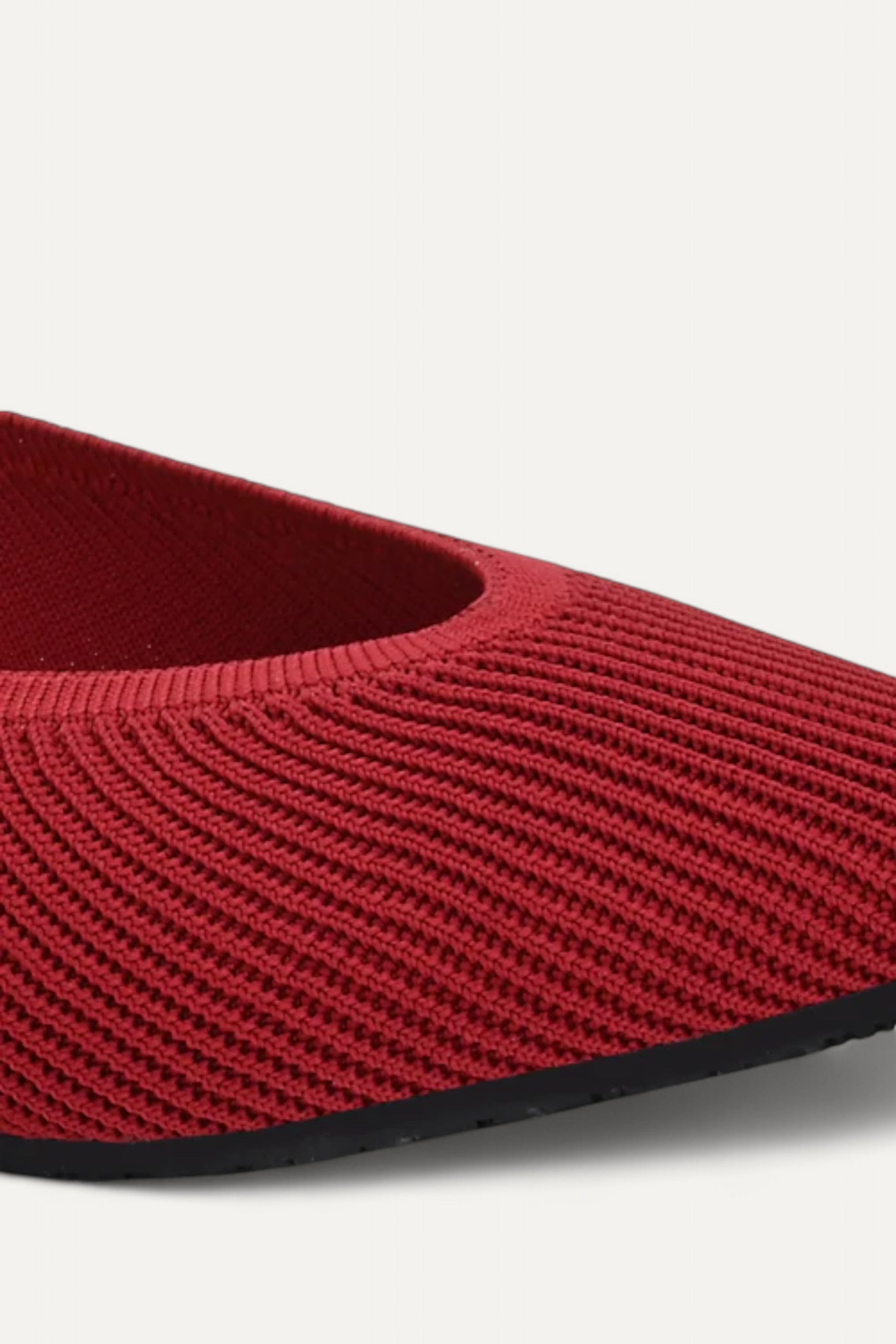 Close-up knit texture of red pointed-toe ballet flat on light gray background