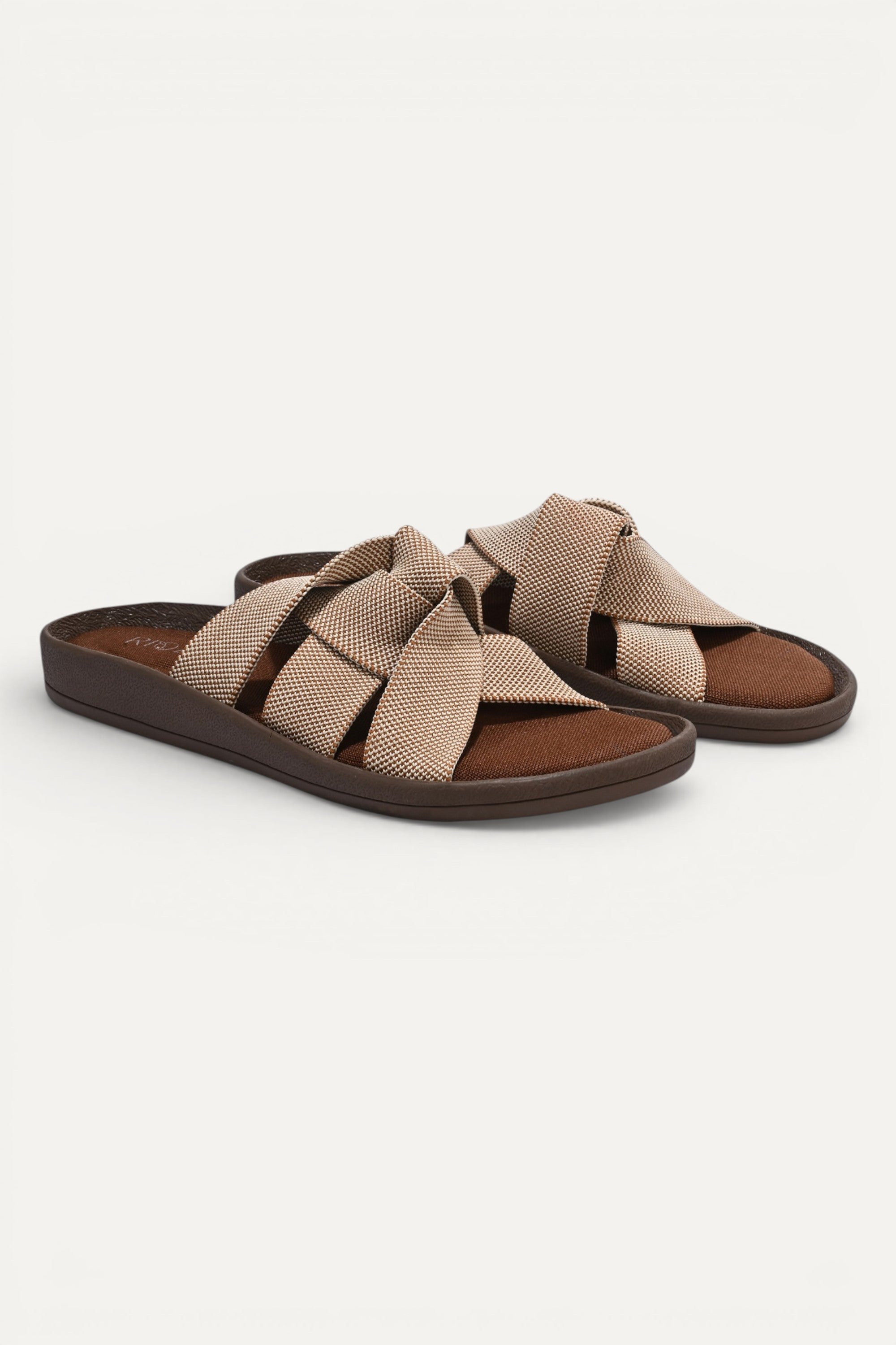 RIOZ eco-friendly slip-on sandals with brown beige woven bow straps, cushioned tan footbed, and brown sole, designed for lightweight everyday comfort and sustainable style.