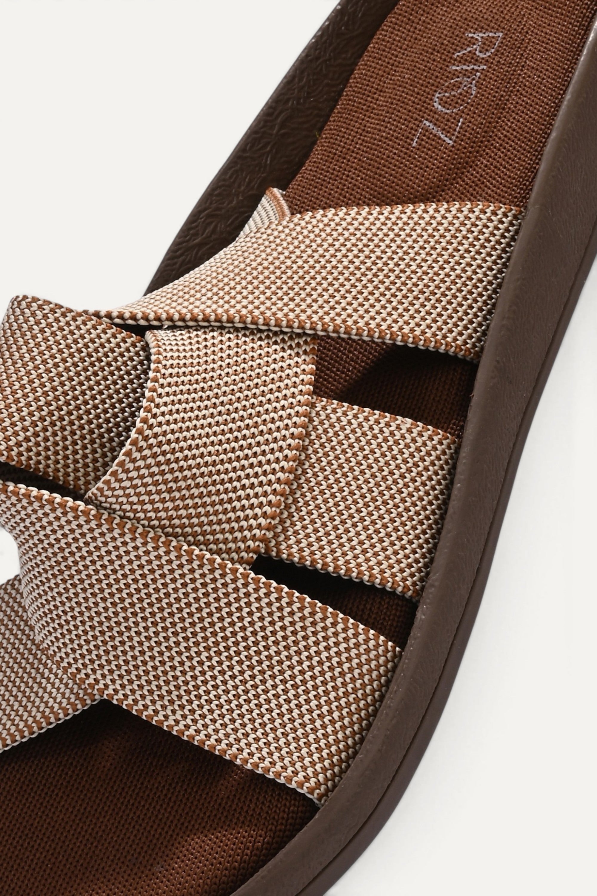 RIOZ eco-friendly slip-on sandals with brown beige woven bow straps, cushioned tan footbed, and brown sole, designed for lightweight everyday comfort and sustainable style.