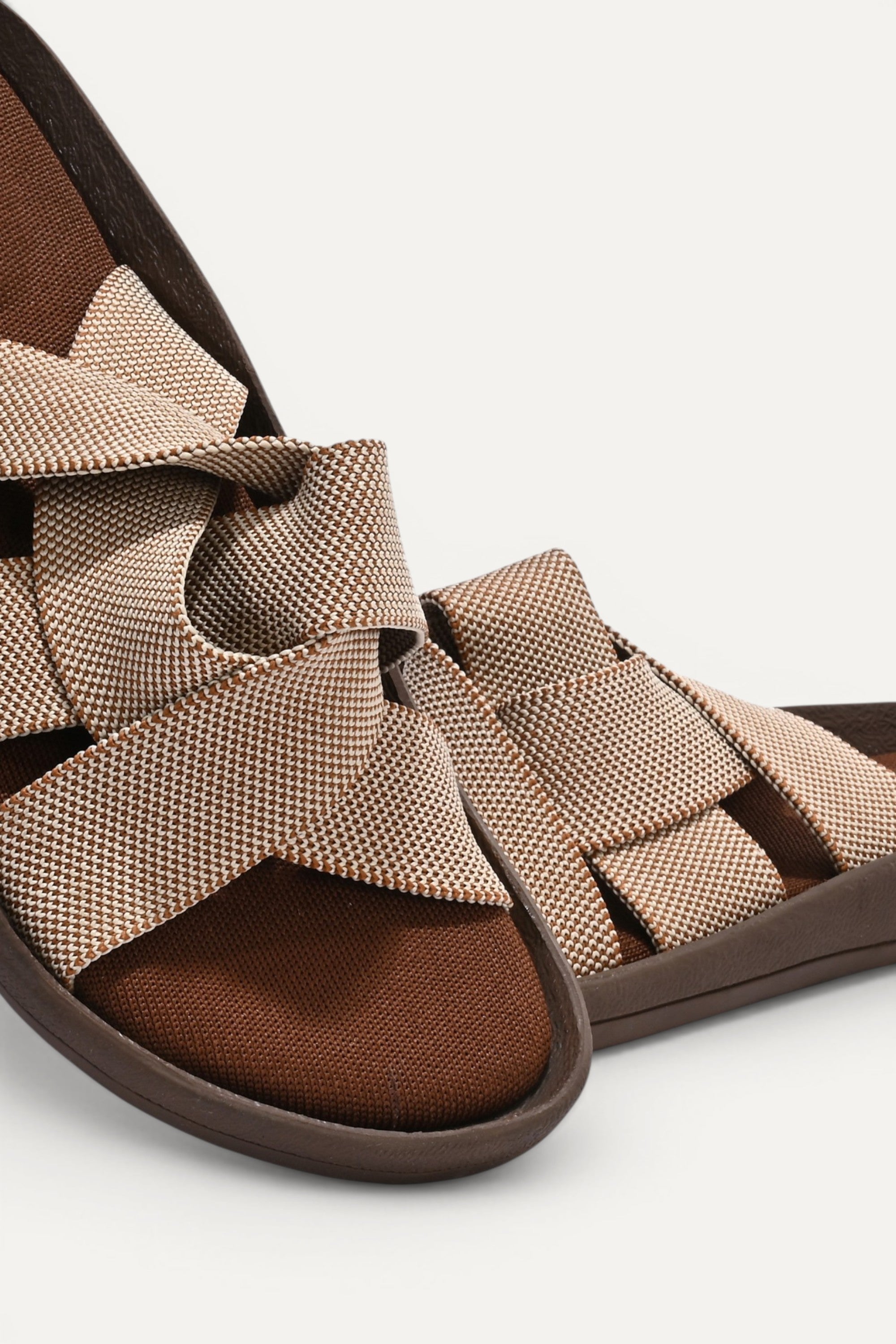 RIOZ eco-friendly slip-on sandals with brown beige woven bow straps, cushioned tan footbed, and brown sole, designed for lightweight everyday comfort and sustainable style.