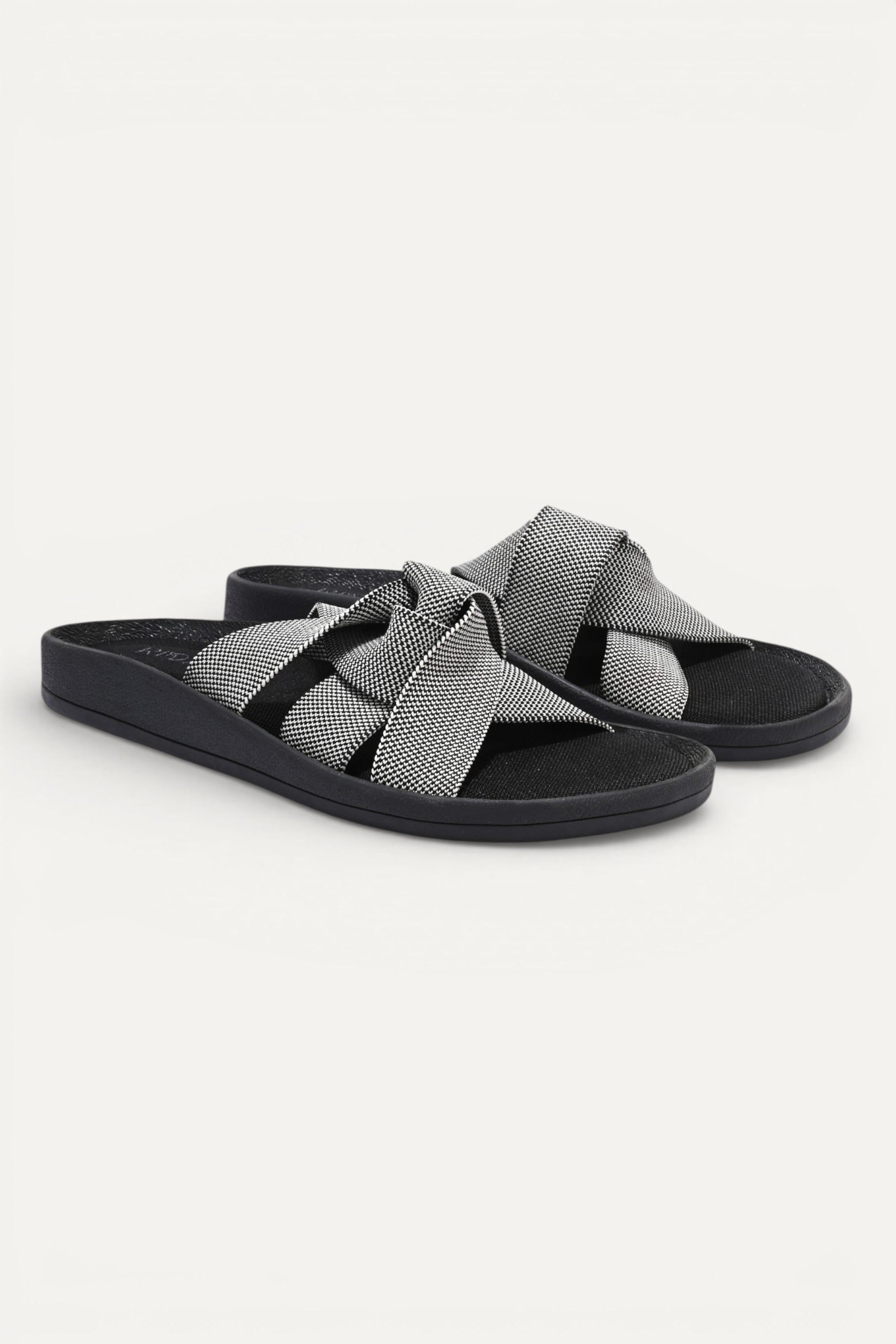 RIOZ eco-friendly slip-on sandals with grey woven bow straps, cushioned tan footbed, and brown sole, designed for lightweight everyday comfort and sustainable style.