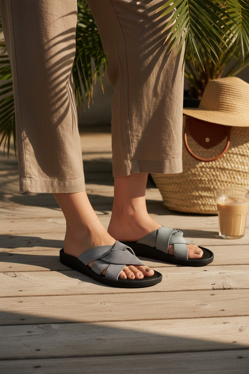 RIOZ eco-friendly slip-on sandals with grey woven bow straps, cushioned tan footbed, and brown sole, designed for lightweight everyday comfort and sustainable style.