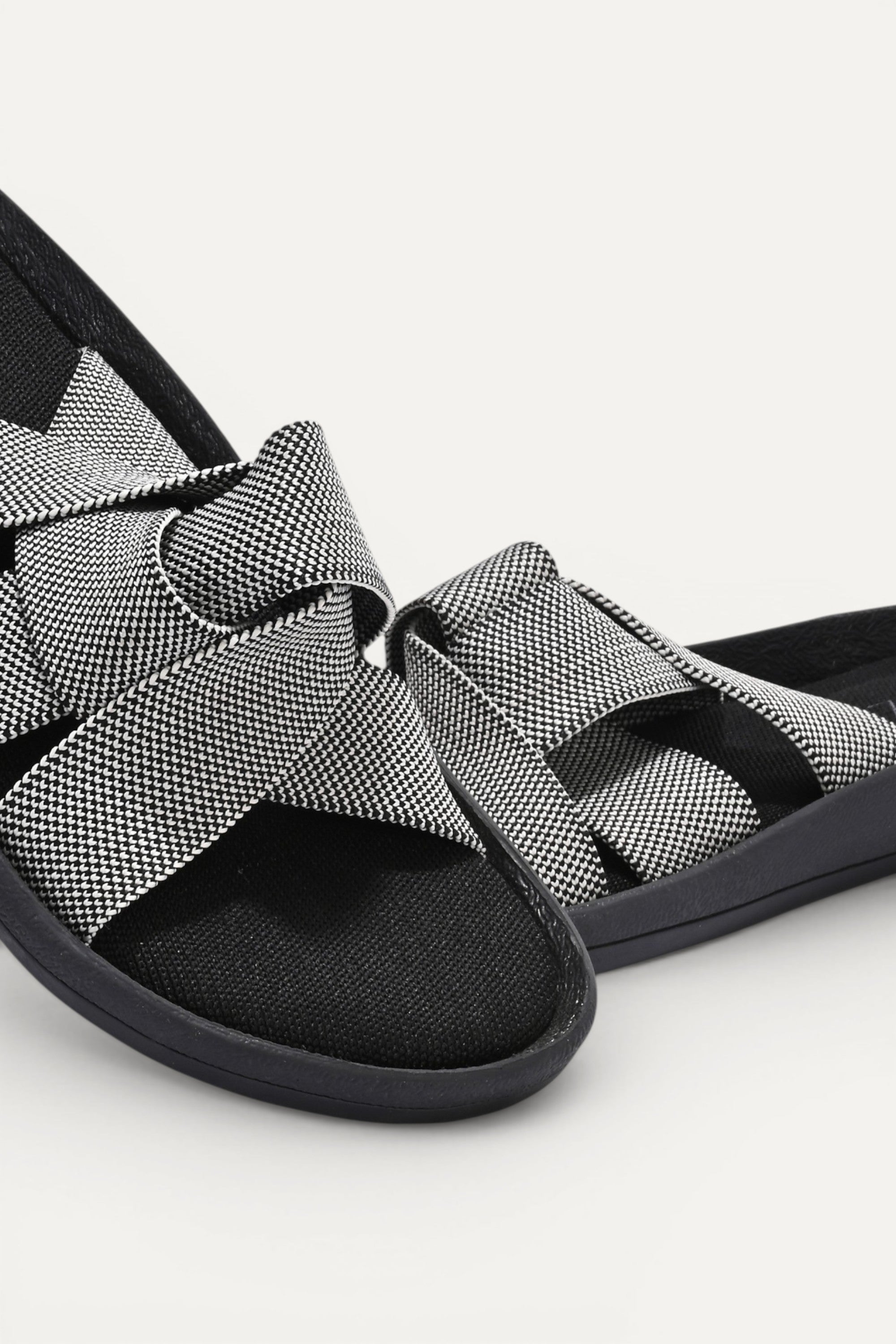 RIOZ eco-friendly slip-on sandals with grey woven bow straps, cushioned tan footbed, and brown sole, designed for lightweight everyday comfort and sustainable style.