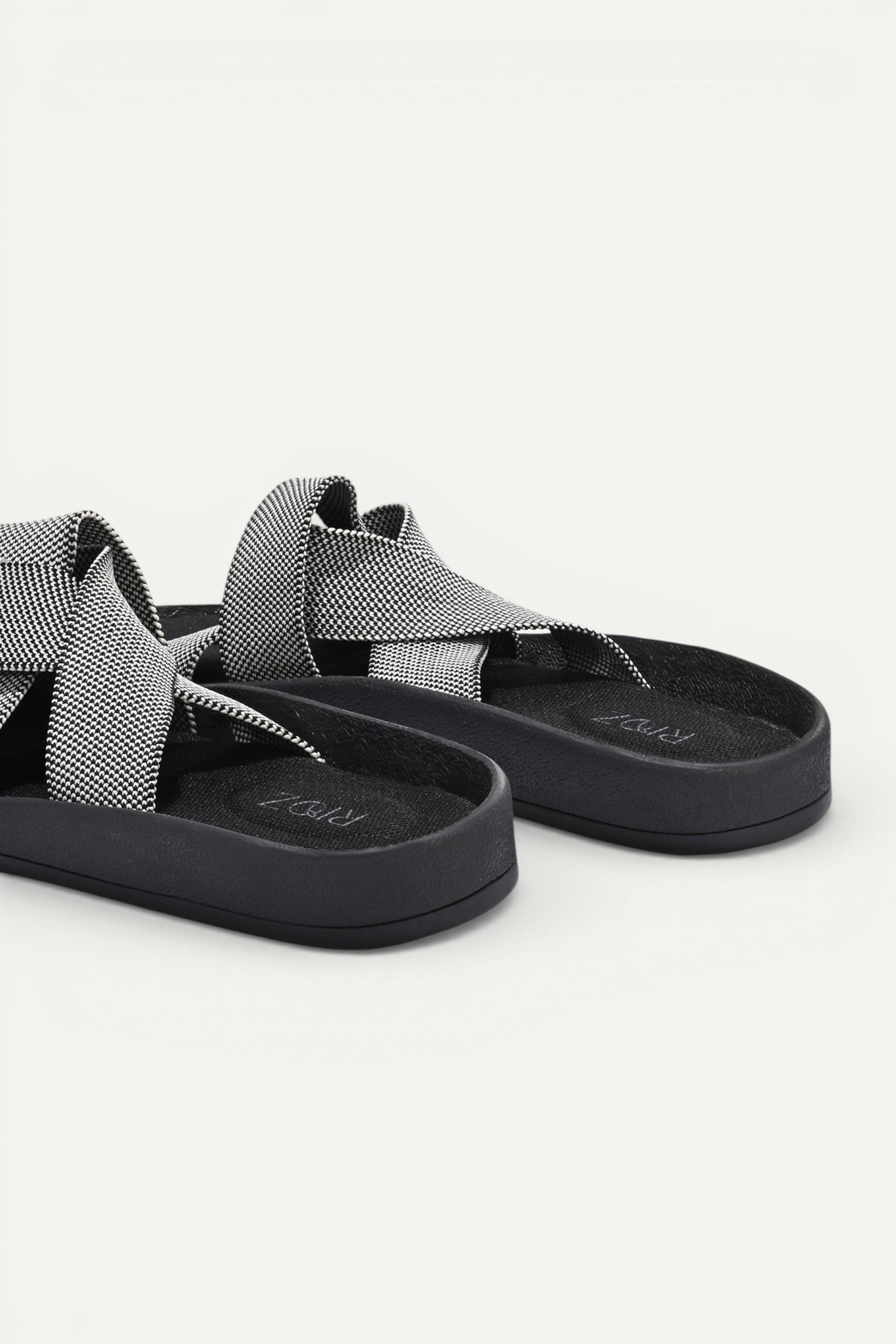 RIOZ eco-friendly slip-on sandals with grey woven bow straps, cushioned tan footbed, and brown sole, designed for lightweight everyday comfort and sustainable style.