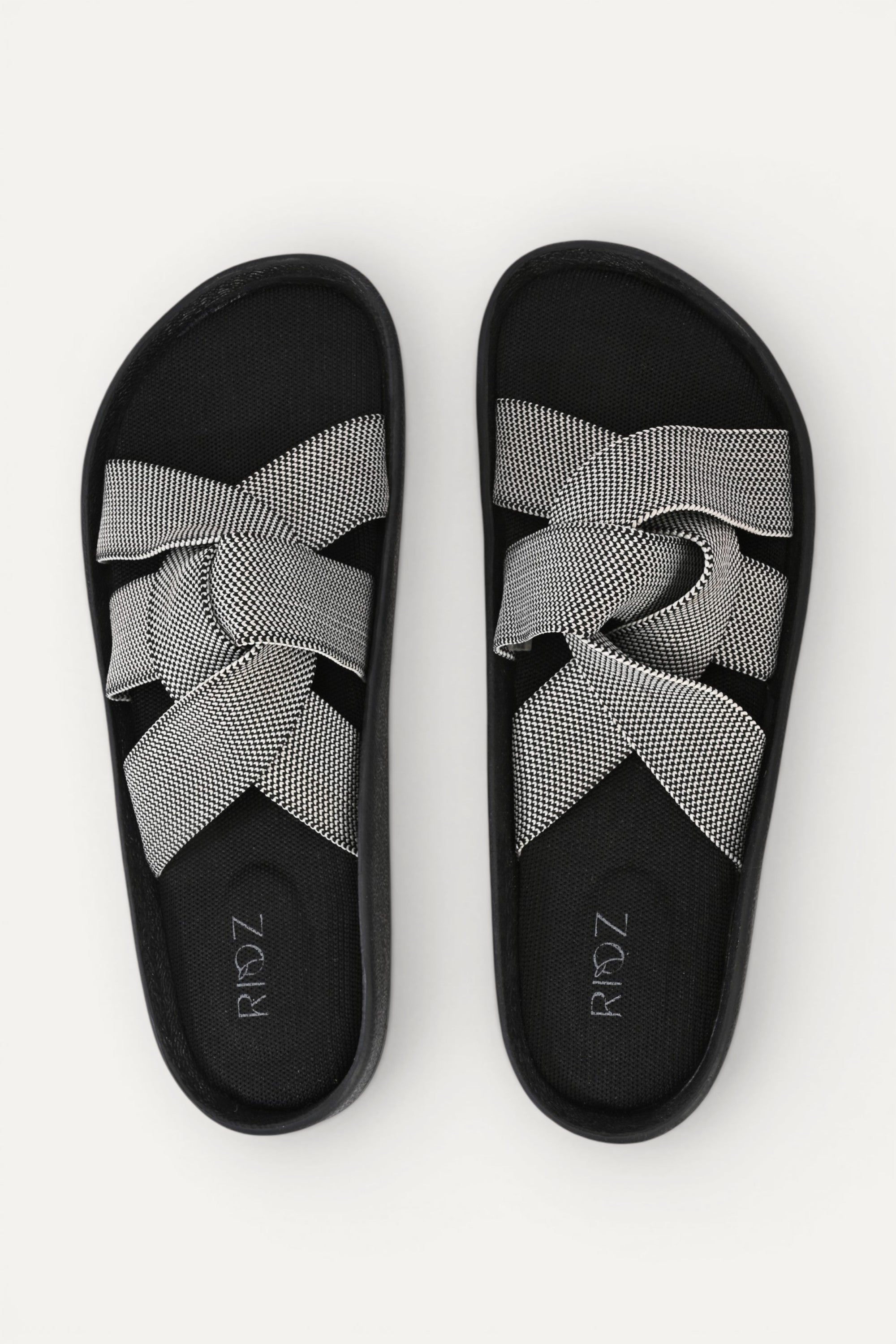 RIOZ eco-friendly slip-on sandals with grey woven bow straps, cushioned tan footbed, and brown sole, designed for lightweight everyday comfort and sustainable style.
