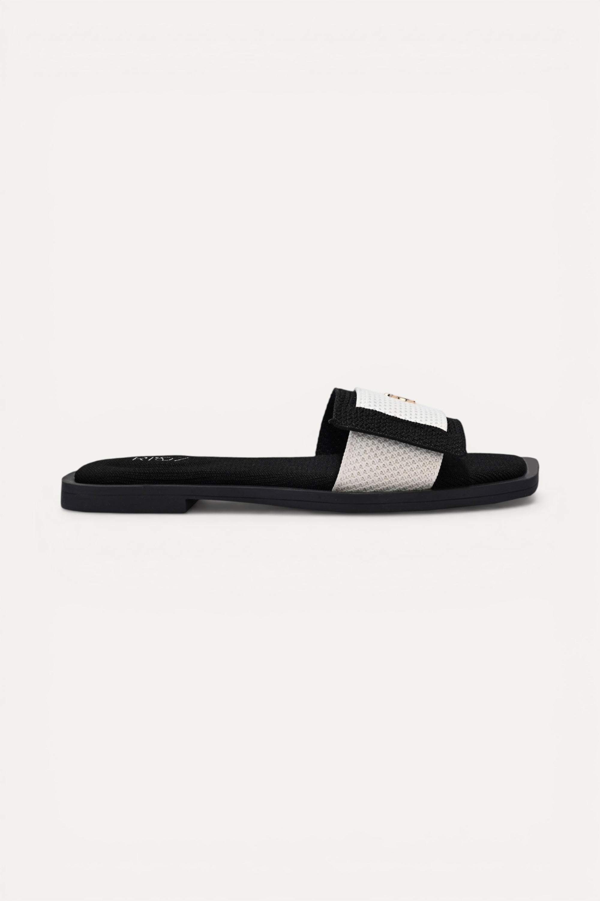 Rioz black and white knit origami slide with gold emblem detail. Asymmetrical fold design, sustainable, 3D-knit, machine washable.