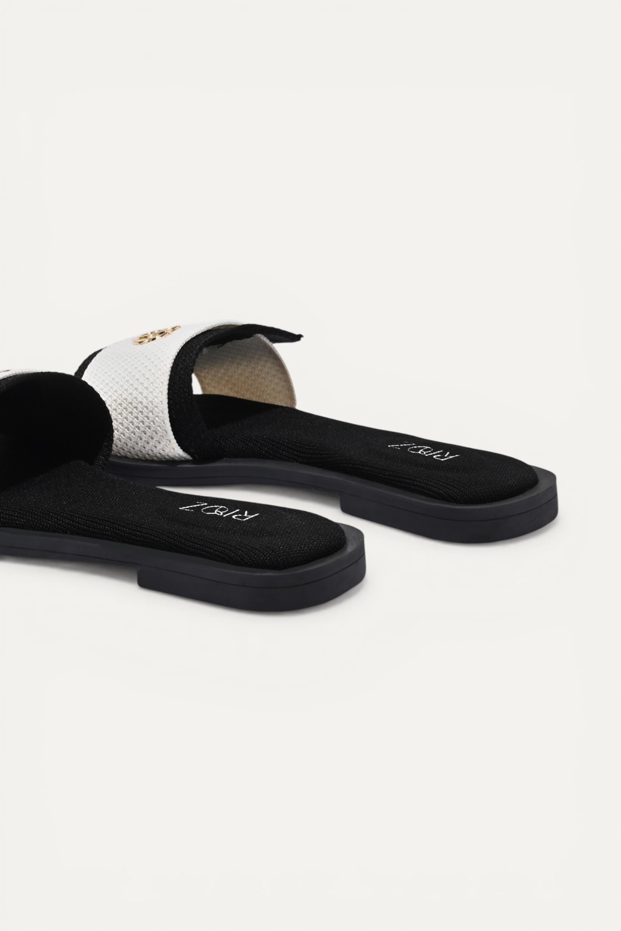 Rioz black and white knit origami slides with gold emblem detail and ergonomic sole.