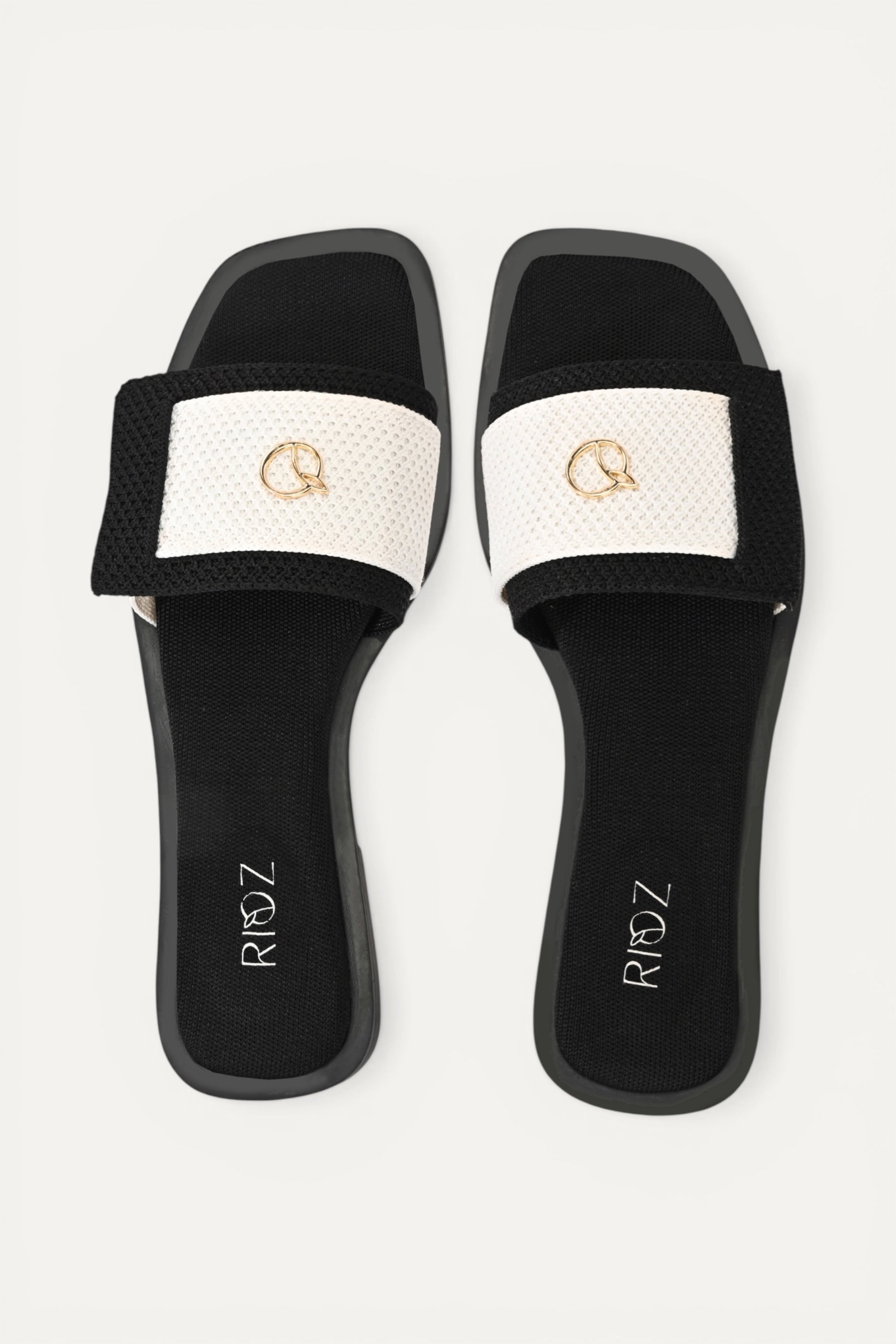 Rioz black knit slides with white asymmetrical strap and gold emblem. Modern, sustainable, and comfortable.