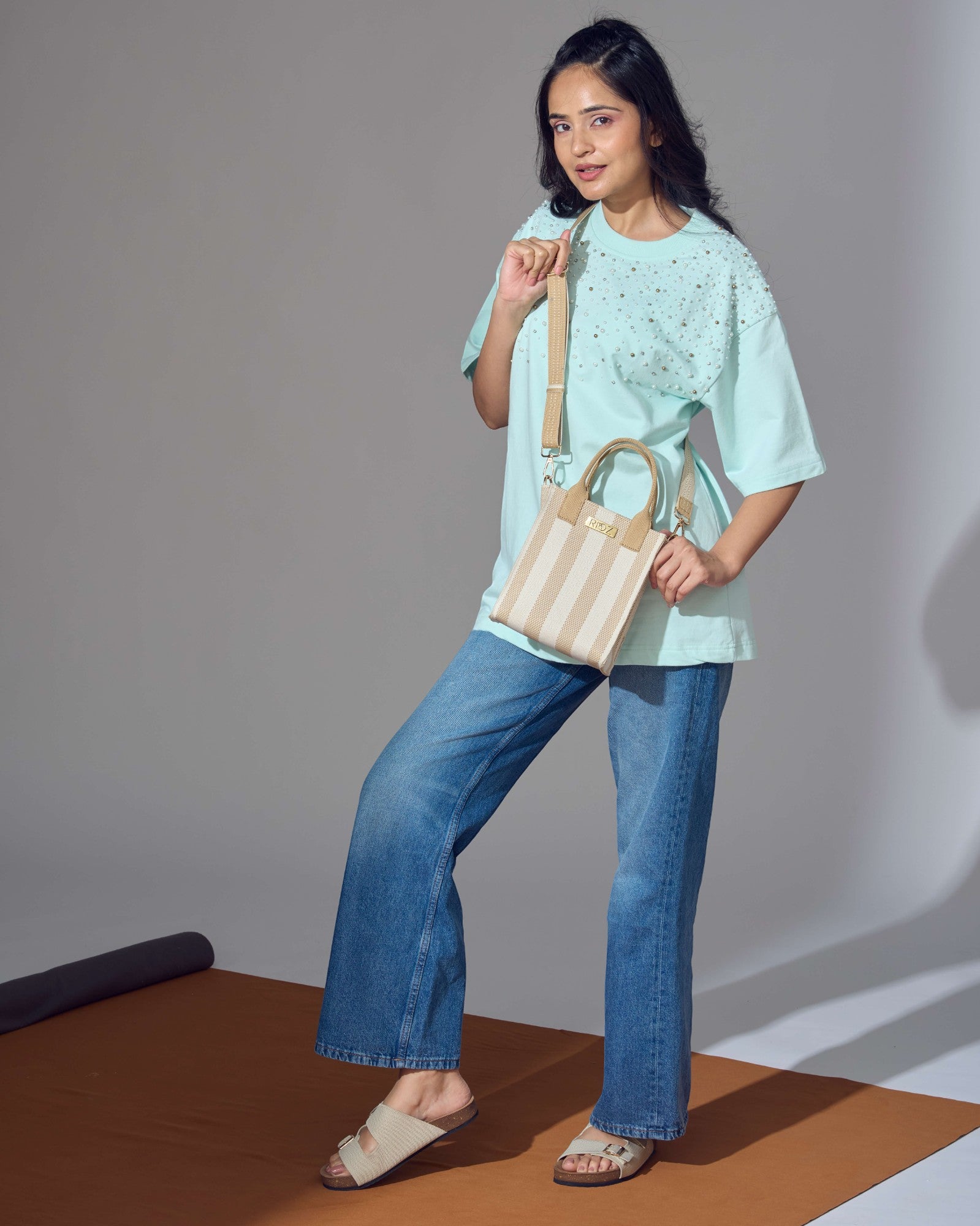 Full-body shot of model wearing the Midday Mini tote bag in ivory and wheat stripes by Rioz; compact, eco-friendly and lightweight crossbody bag for daily essentials.